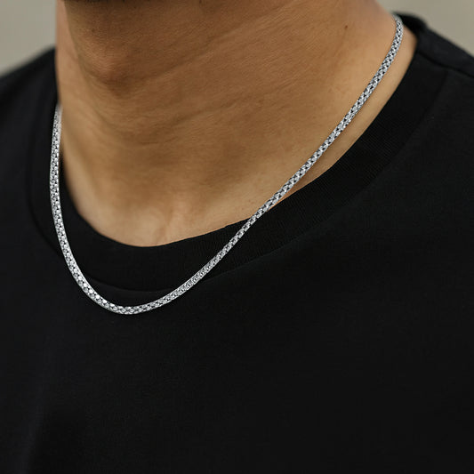 Silver crub chain necklace worn by a person on a plain background