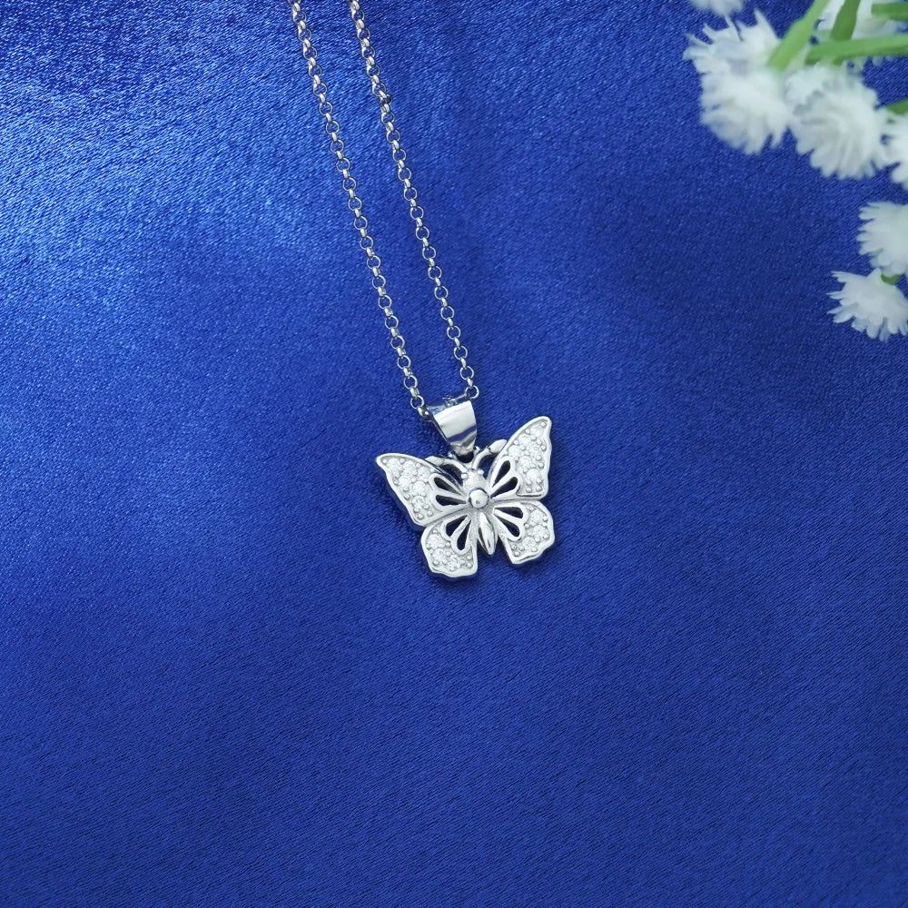 Silver butterfly pendant necklace on a blue fabric background with white flowers.