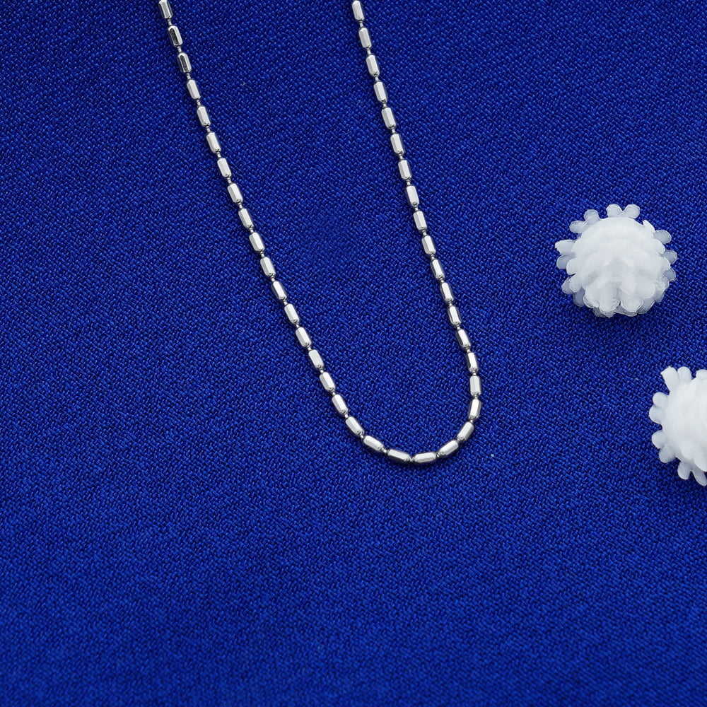 Silver beaded necklace on a blue fabric background with white spherical objects.