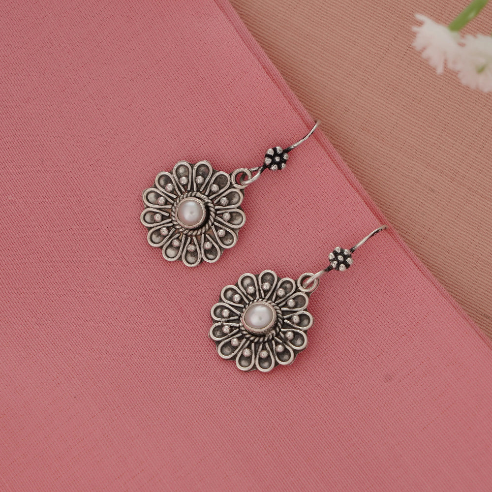Silver floral earrings with pearl center on a pink fabric background