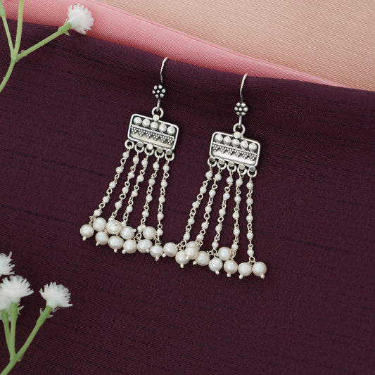 Silver hanging earrings with pearl-like beads on a dark purple surface with white flowers.