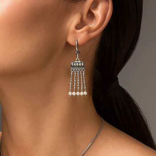Close-up of a woman wearing a silver hanging earring with pearl-like beads against a neutral background