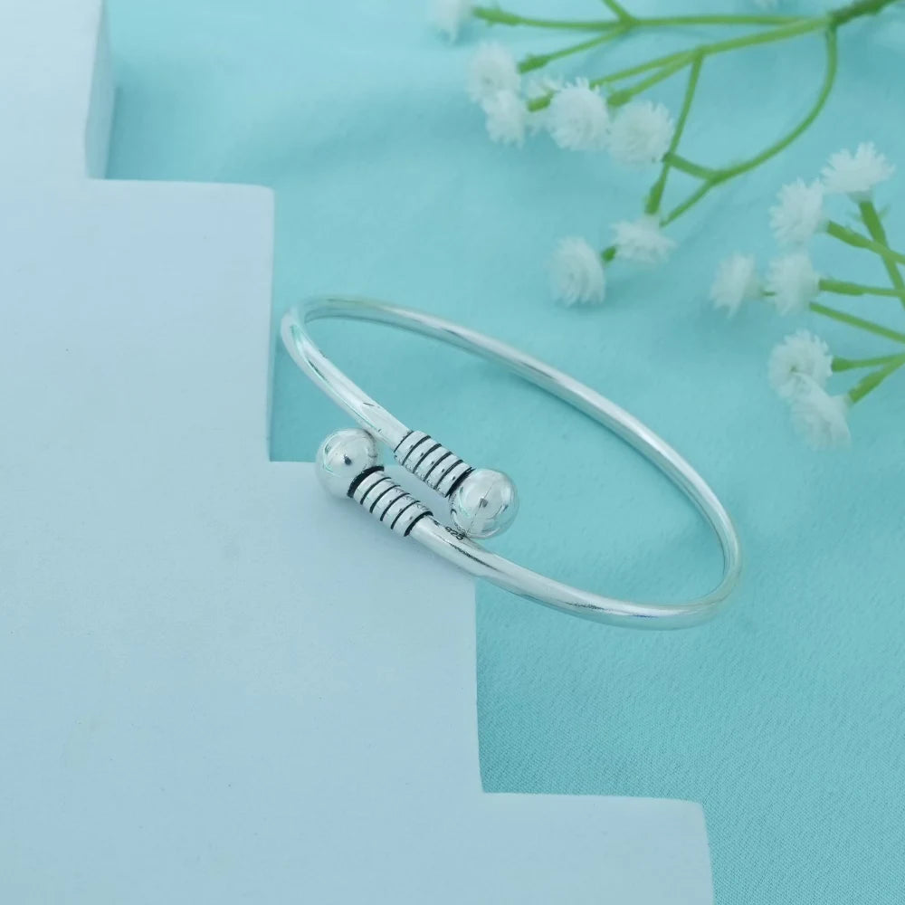 Silver bracelet with decorative beads on a light blue background with white flowers.