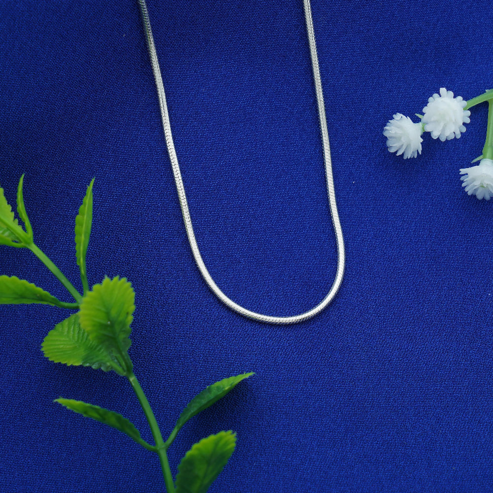 Silver necklace on a blue fabric background with green leaves and white flowers.