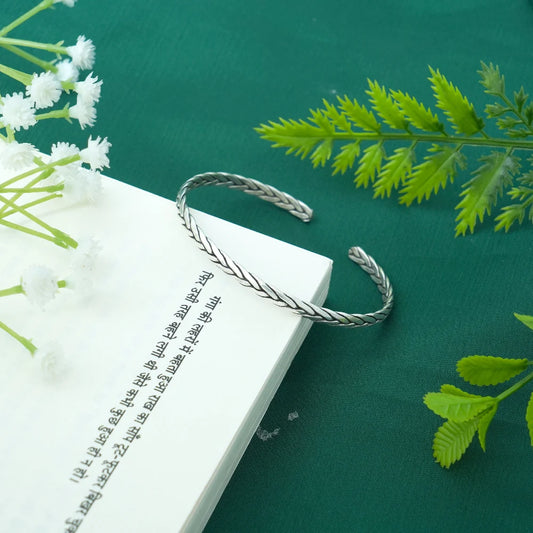 Silver bangle on an open book with white flowers and green leaves on a green background