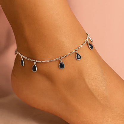 Silver anklet with black teardrop charms on a person's ankle against a peach background