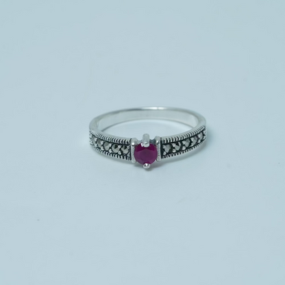 Silver ring with a heart-shaped purple gemstone on a light gray background