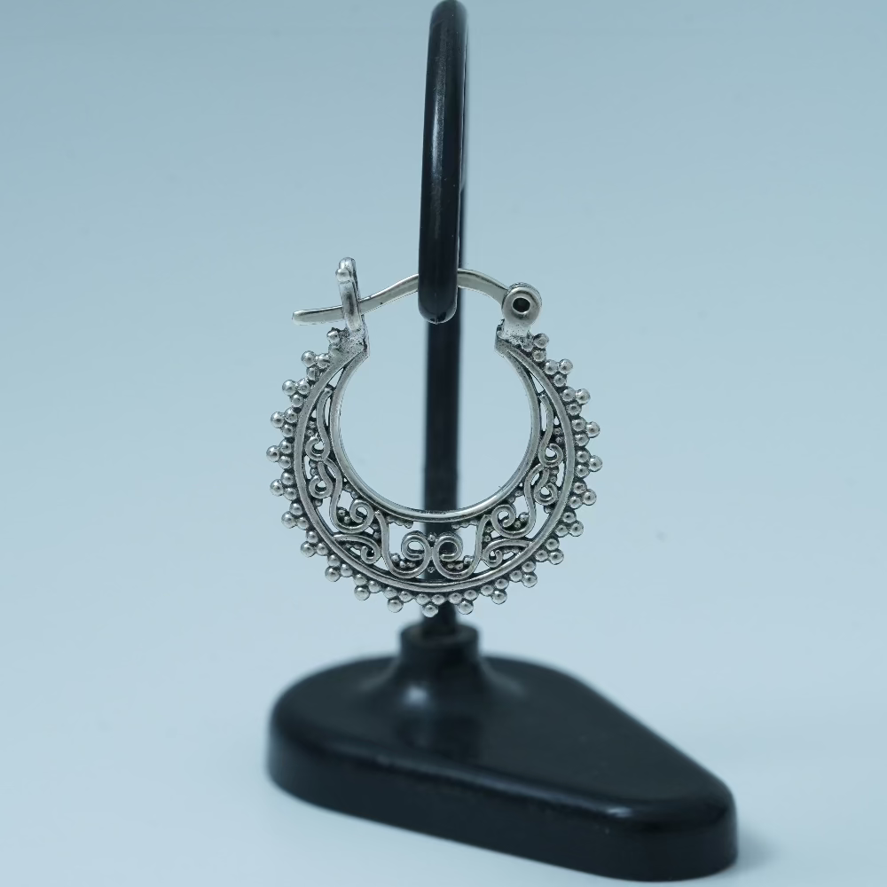 Decorative silver hoop earring on a black stand against a light blue background