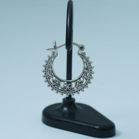 Decorative silver hoop earring on a black stand against a light blue background