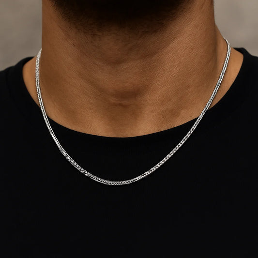 Silver chain necklace on a person wearing a black shirt against a neutral background