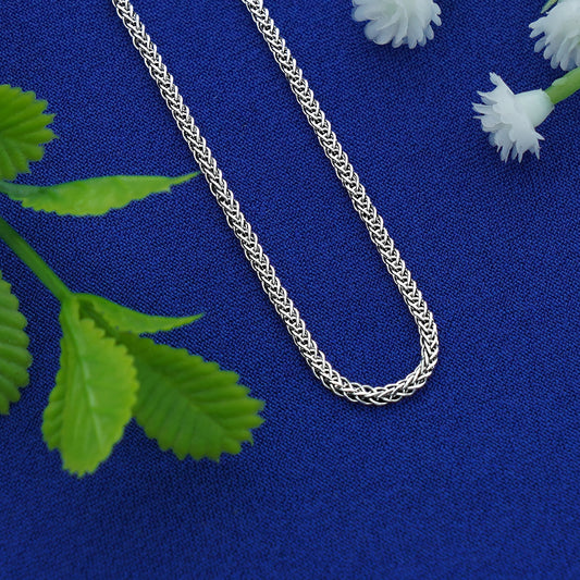 Silver chain necklace on a blue fabric background with green leaves and white flowers.
