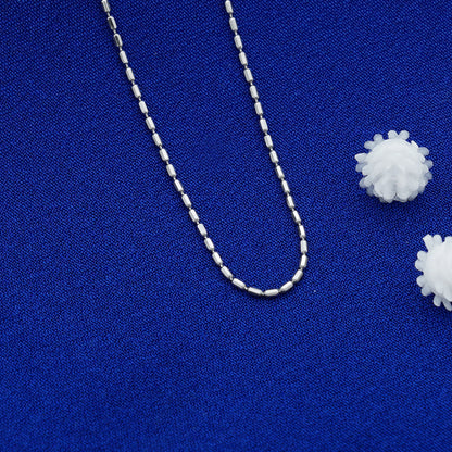 Silver beaded necklace on a blue fabric background with white spherical objects.