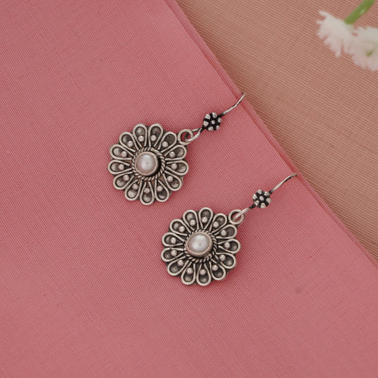 Silver floral earrings with pearl center on a pink fabric background